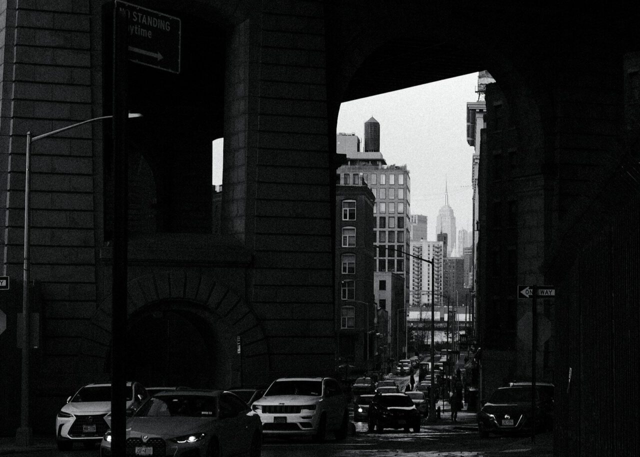 Cars on a street under a bridge with city skyline.